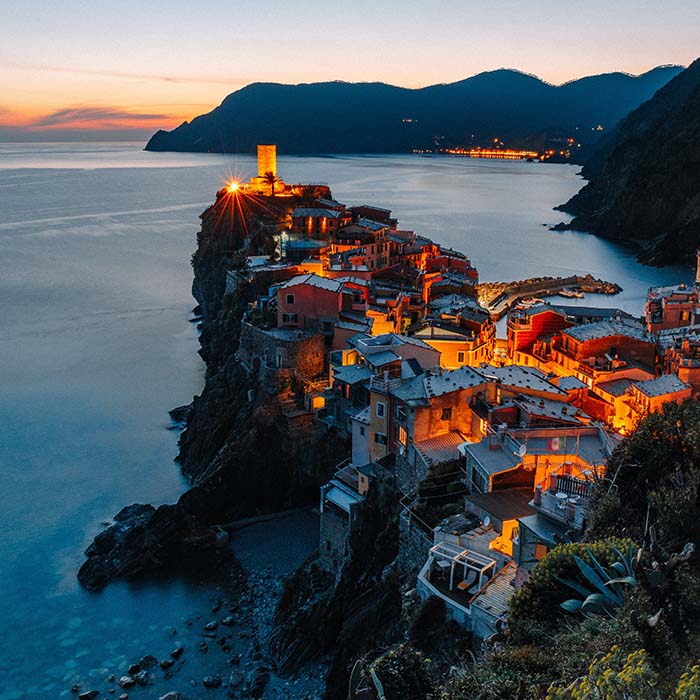sunset photo of a town built ontop of a rock jutting out into the ocean